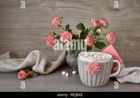Valentines day still life with cup of hot chocolate with marshmallows, pink roses, greeting card and decorations Stock Photo