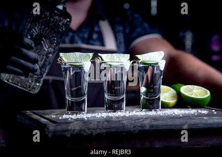 aperitif with friends in the bar, three glasses of alcohol with lime and salt for decoration. Tequila shots, selective focus. Stock Photo