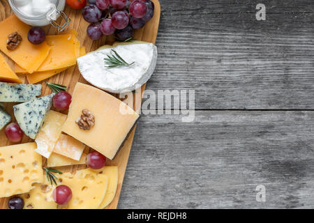 Assorted cheeses on wooden board plate served with walnuts, grapes and rosemary on rustic wood background, top view with copy space Stock Photo