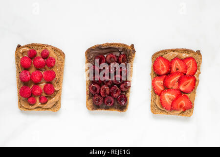 Toast bread with peanut butter and chocolate spread with berries on white marble table. healthy breakfast. top view Stock Photo