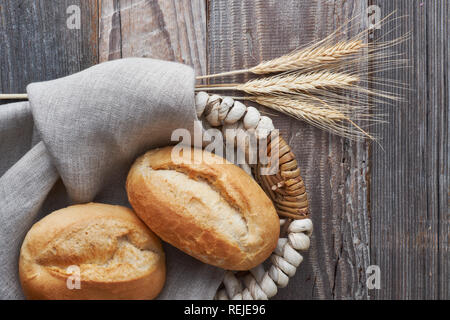 Bread buns in basket on rustic wood with wheat ears, top view Stock Photo