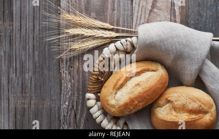 Bread buns in basket on rustic wood with wheat ears, top view Stock Photo