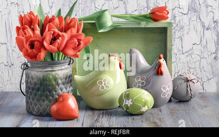Easter arrangement with bunch of red tulips, ceramic hens and Easter eggs on light wooden background Stock Photo