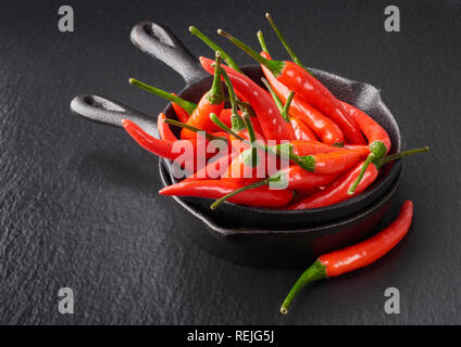Closeup on red hot chili peppers in a stack of two grey ceramic bowls on black slate stone background Stock Photo