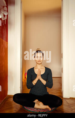 Pretty young woman yoga instructor meditating sitting on a rug on the floor in a black solid suit getting ready for a great workout. Toned image. Stock Photo