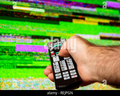 Man with large tv remote trying to fix the digital television noise on a large plasma OLED 4K Ultra HD High Dynamic Range HDR Smart TV . Stock Photo
