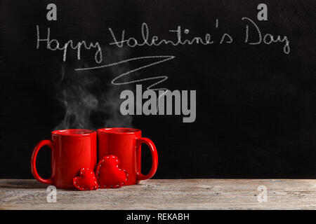 Happy Valentine's Day text with white chalk on black blackboard and two tea mugs Stock Photo