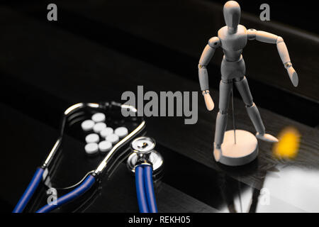 Pills, a stethoscope and a fake person on a black background Stock Photo