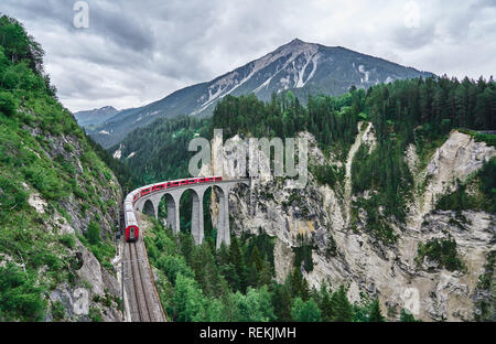 Red train passes above the Landwasser Viaduct bridge, in canton of Graubünden, Switzerland. Bernina Express / Glacier Express uses this railroad. Stock Photo