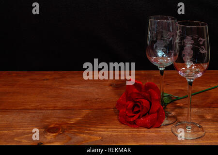 Beautiful etched wine glasses with a single red rose on wooden table and dark background. Valentines, Mothers Day, Easter, Christmas, Wedding Concepts Stock Photo