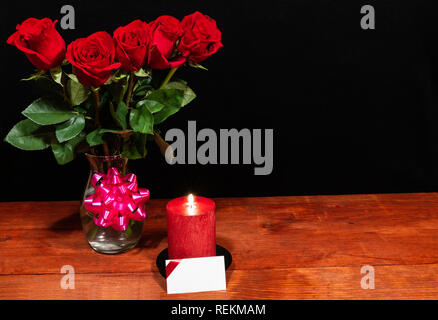 Beautiful red roses in vase with pink bow and red candle with name tag on wooden table on dark background. Valentines, Mothers Day, Easter, Christmas, Stock Photo