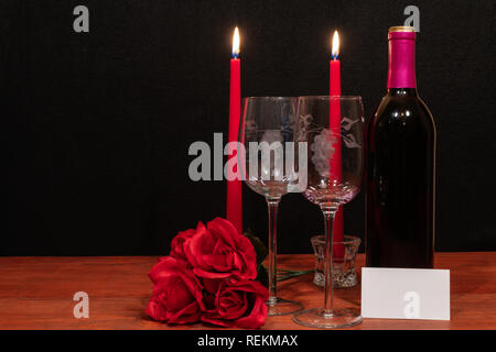 Beautiful etched wine glasses and bottle of red wine, red candles and red roses on wooden table with name tag on dark background. Valentines, Mothers  Stock Photo