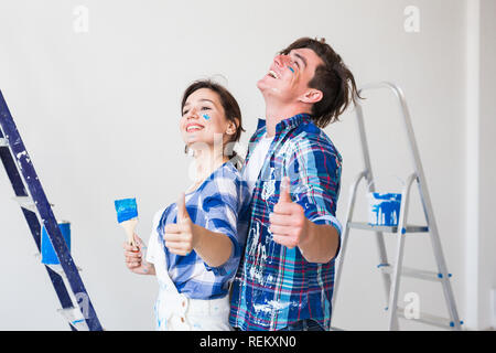 Redecoration, renovation and love couple concept - young man and woman in love and painting the wall, showing thumbs up Stock Photo