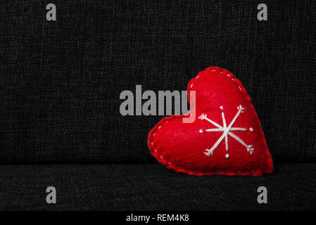 Red valentines day heart with white ornaments or snowflake made from wool on dark fabric background. Concept of love, warmth and christmas Stock Photo