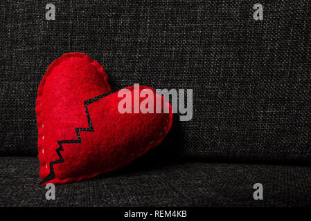 Broken red valentines day heart made from wool on dark fabric background. Split in two parts. Concept of heartbrake, end of relationship and divorce. Stock Photo