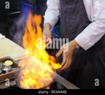 Chef in restaurant kitchen at stove with pan, doing flambe on food Stock Photo