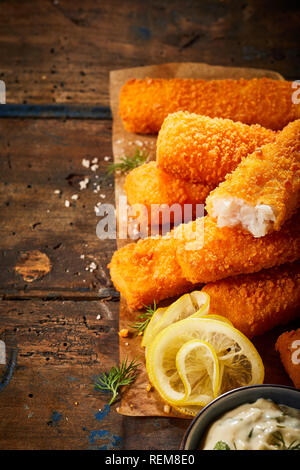 Golden oven baked crumbed fish sticks made from hake or whitefish served on paper with lemon and tartare sauce Stock Photo