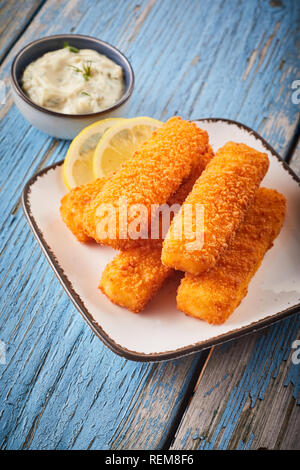 Crispy breaded fish fingers with tartare sauce to the side served on a plate on rustic weathered blue wood in a high angle view Stock Photo