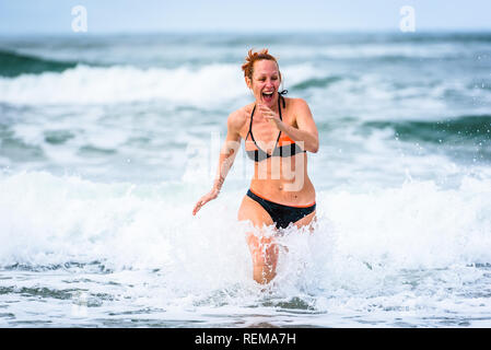 Woman enjoying the sea and waves of Atlantic ocean. Mature, mid aged, young attractive woman in bathing suit bikini is running in the ocean sea, playi Stock Photo