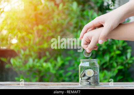 Little girl and pile coin for saving. money saving concept. girl and mother putting coins into glass bottle. To have a good future both in education a Stock Photo