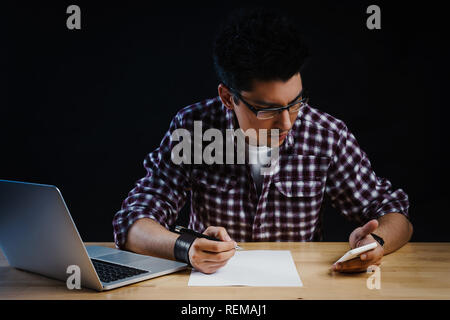 Programmer in the office working on the computer and writes on a piece of paper Stock Photo