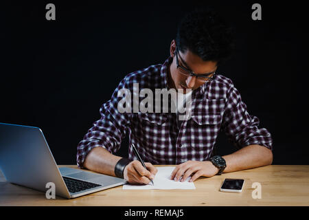 Programmer in the office working on the computer and writes on a piece of paper Stock Photo