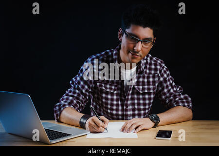 Programmer in the office working on the computer and writes on a piece of paper Stock Photo
