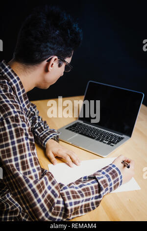 Programmer in the office working on the computer and writes on a piece of paper Stock Photo