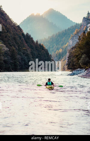 Young man kayaking on the Dunajec river, sitting in a kayak and paddling down the river. Enjoying ride surrounded by hills and beautiful view of valle Stock Photo