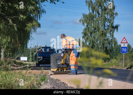 Manual road repair vibrating machine being pushed by a worker during road construction work on gravel road curbs. Road repairing in city. Heavy machin Stock Photo
