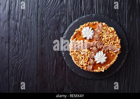 peanut cake topped with cocoa peanut butter cream and egg whites roses on a stone plate on a wooden table, view from above, copy space, flatlay Stock Photo