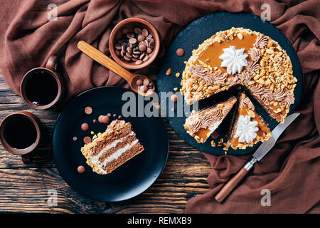 peanut cake topped with cocoa peanut butter cream and egg whites roses served on a black plate on a rustic wooden table with coffee in earthenware cup Stock Photo