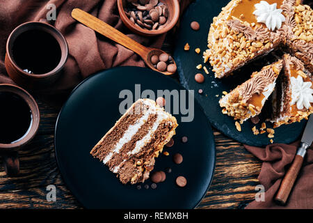 peanut cake topped with cocoa peanut butter cream and egg whites roses served on a black plate on a rustic wooden table with coffee in earthenware cup Stock Photo