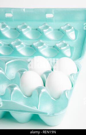 Four raw white chicken eggs in a brightly-colored 18-slot egg-shape styrofoam container. Stock Photo