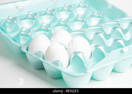 Four raw white chicken eggs in a brightly-colored 18-slot egg-shape styrofoam container. Stock Photo
