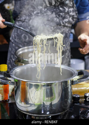 Chef takes out with slotted spoon hot steaming egg noodles from pan Stock Photo