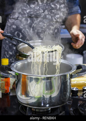 Chef takes out with slotted spoon hot steaming egg noodles from pan Stock Photo