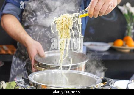 Chef takes out with slotted spoon hot steaming egg noodles from pan Stock Photo