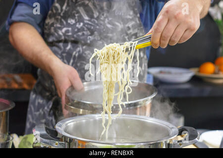 Chef takes out with slotted spoon hot steaming egg noodles from pan Stock Photo