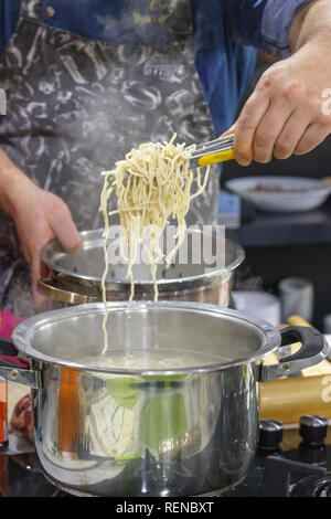 Chef takes out with slotted spoon hot steaming egg noodles from pan Stock Photo
