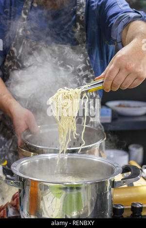 Chef takes out with slotted spoon hot steaming egg noodles from pan Stock Photo