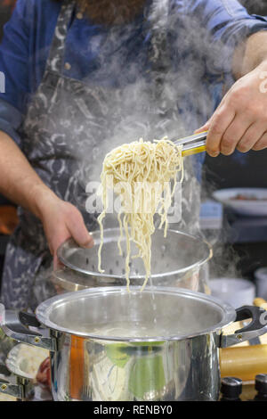 Chef takes out with slotted spoon hot steaming egg noodles from pan Stock Photo