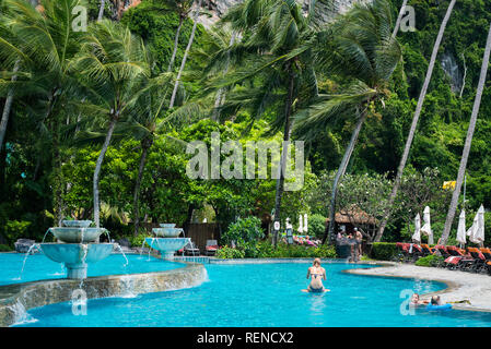 Ao Nang, Thailand - July 2, 2018: a blue pool with tourists in it below coconut trees that sway in the wind. Stock Photo
