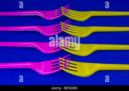Yellow and pink cutlery plastic forks arranged on blue background. Color trends and plastic waste problem concept Stock Photo