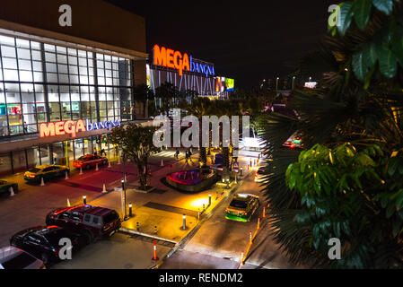 Bangkok, Thailand - August 17, 2018: Mega Bangna Shopping Mall exterior at night with a street (parked cars, taxis, trees, people walk) in front of it Stock Photo