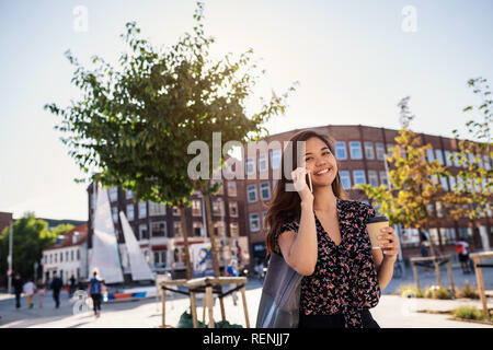 Smiling Asian collage student walking and talking on her cellphone Stock Photo