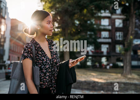 Young Asian businesswoman standing outside after work using her cellphone Stock Photo