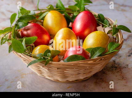 Easter eggs in the basket. Easter eggs on marble background. A sprig of greenery. Colorful easter eggs in a basket. Stock Photo