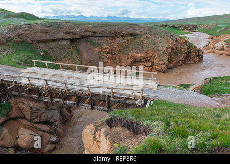 Wooden bridge over a muddy river flowing in a wild gorge, Naryn Province, Kyrgyzstan Stock Photo