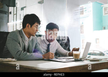 Two asian business men working together in a coffee shop. Business colleagues sitting at coffee shop table analysing some documents.